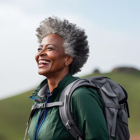 Lachende Frau mit Rucksack in der Natur | Rucking: Darum ist dieser simple Fitnesstrend effektiver als Joggen