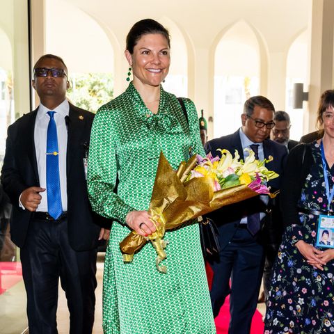 Kronprinzessin Victoria von Schweden besucht Bangladesch in einem verspielten und eleganten Maxikleid von Dea Kudibal. Während ihres viertägigen Besuchs erscheint sie als Sonderbotschafterin des Entwicklungsprogramms der Vereinten Nationen (UNDP). Zu ihrem grünen Kleid trägt sie passende Ohrringe mit farblich passenden Steinen und schwarze Pumps.