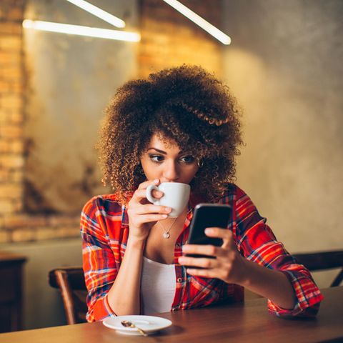 Frau trinkt Kaffee und schaut aufs Telefon: Schadet Stress unserer Intelligenz?