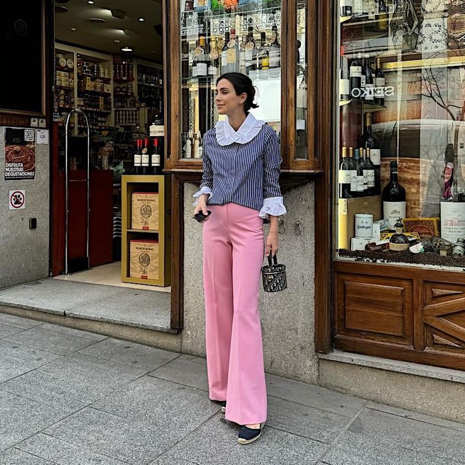 Verspielte Eleganz zeigt uns Alessandra de Osma beim Sonntagspaziergang durch Madrid. Zur blau-weißgestreiften Bluse mit rüschigem Kragen von Maria de la Orden trägt die Prinzessin eine rosafarbene Marlene-Hose, schwarze Espandrilles mit luxuriösem Kosmetikkoffer-Täschchen von Dior, mit ca. 2.585 Euro nicht ganz ein Schnäppchen.