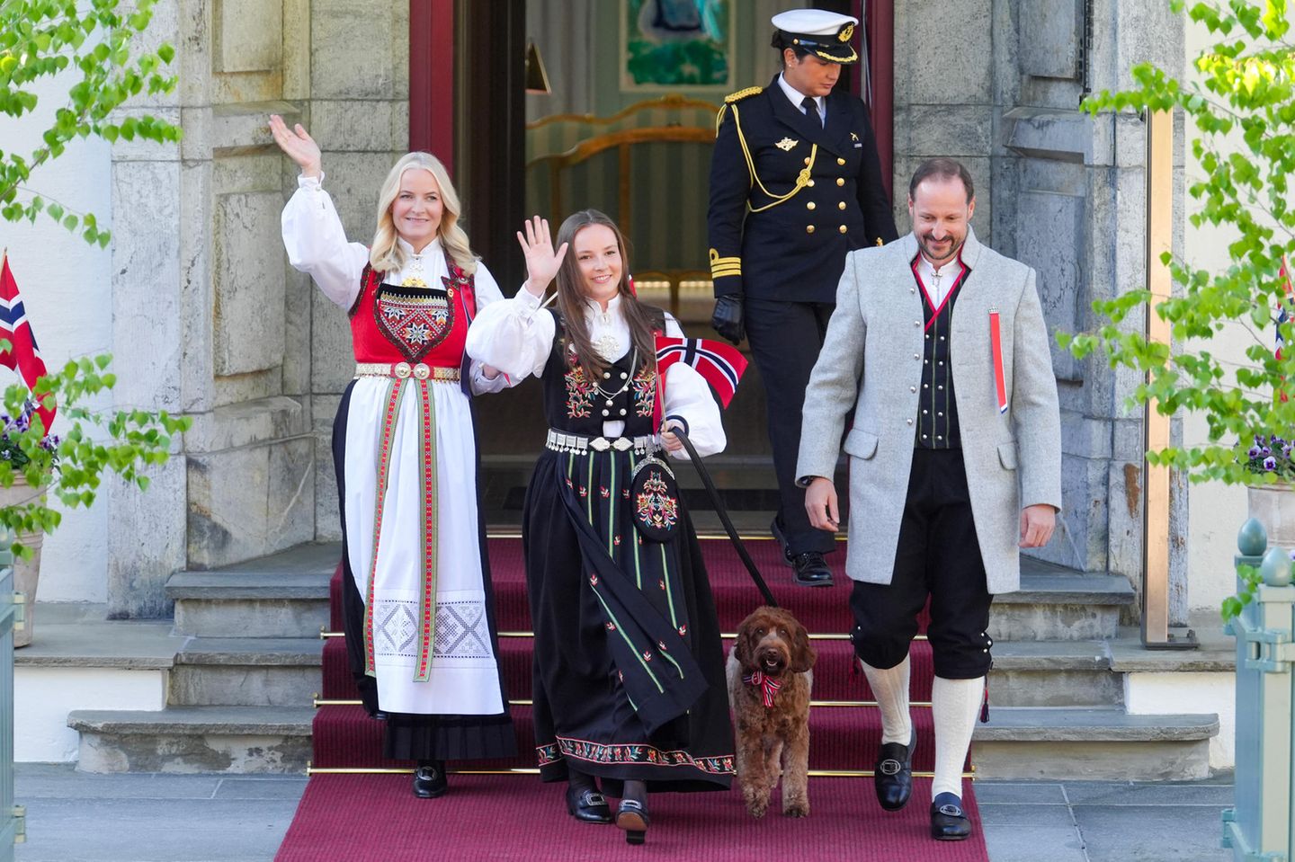 Es ist so weit! Pünktlich zum traditionellen Kinderumzug auf Gut Skaugum in Asker kommen Prinzessin Mette-Marit, Prinzessin Ingrid Alexandra und Prinz Haakon vor die Tür, um die Kinder zu begrüßen. Familienhund Molly darf natürlich nicht fehlen und wird von Ingrid Alexandra an der Leine geführt.