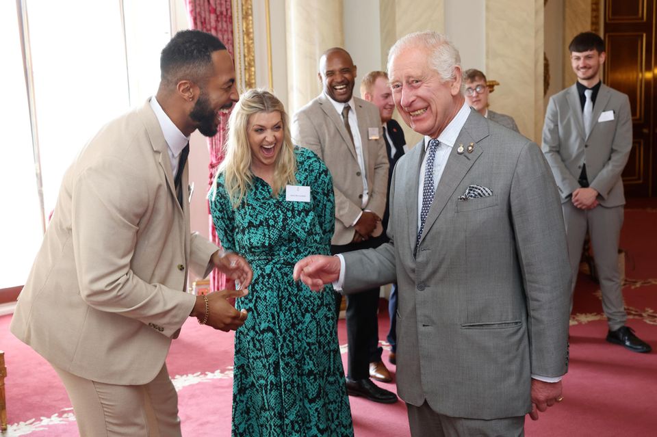 König Charles erwidert die informelle Geste zur Begrüßung und bringt damit den ganzen Saal zum Lachen. 