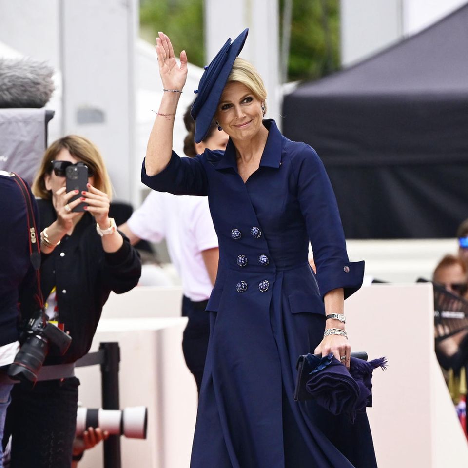 Bei der Gedenkfeier anlässlich des 80. Jahrestags der alliierten Landung in der Normandie setzt Königin Máxima auf ihr Maison-Natan-Mantel-Kleid, das sie zur Clutch der gleichen Marke kombiniert. Ihr Ton-in-Ton-Motto verfolgt sie auch weiterhin bei ihren Gianvito-Rossi-Pumps – auch diese wählt die Dreifach-Mama in Blau. Der seitlich angebrachte Hut vervollständigt den klassischen Royal-Style, der mit einem kostspieligen Highlight glänzt: Máximas Uhr von Patek Phillipe aus Weißgold ist mit Diamanten bestückt und stammt aus den 1990er Jahren. Heute wird sie für rund 12.000 Euro gehandelt.