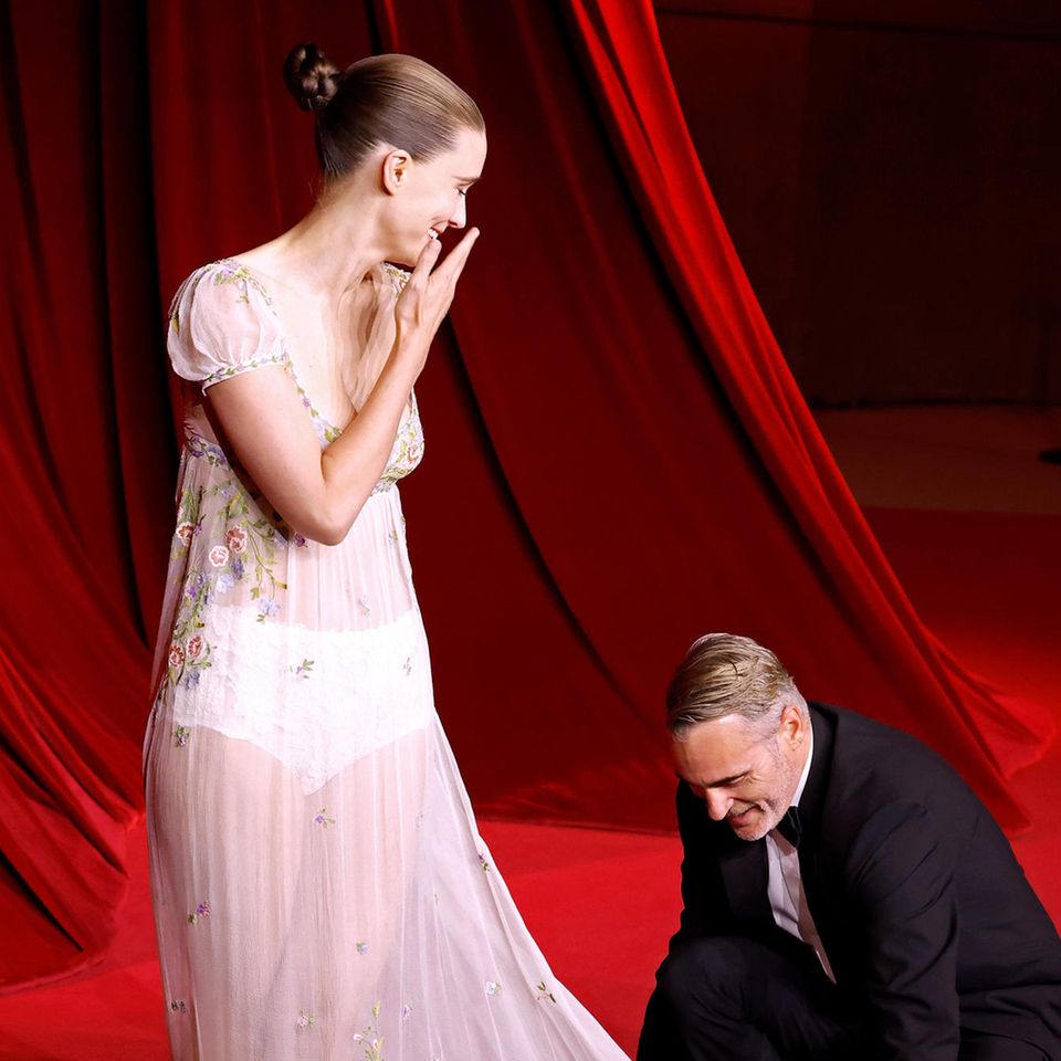  Joaquin Phoenix kniet sich vor Rooney Mara hin, um ihre Schleppe zurechtzulegen.