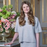 Prinzessin Estelle trägt bei ihrem Geburtstagsfotoshooting ein graues, kurzärmliges Oberteil, zu dem sie einen passenden Rock kombiniert. Um den Hals trägt sie eine goldene Kette mit Herzanhänger, an ihrem Handgelenk baumelt ein Perlenarmband. 