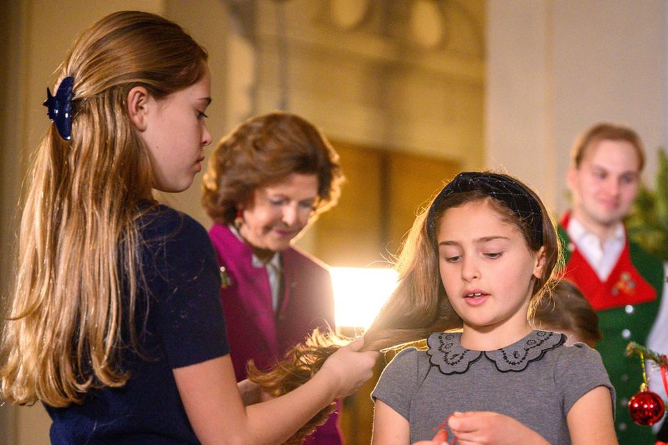 Prinzessin Leonore kümmert sich um Prinzessin Adriennes Haare, während sie den Weihnachtsbaum schmückt